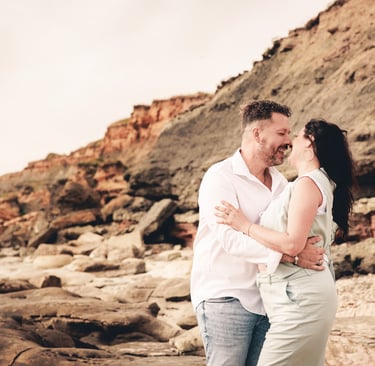 un homme et une femme debout sur des rochers devant une falaise