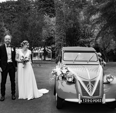 Un couple de mariés posant à côté d'une voiture ancienne