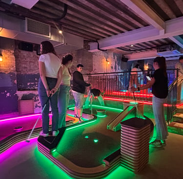 Estudiantes jugando al minigolf en un local de ocio iluminado con luces de neón
