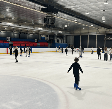 Un grupo de estudiantes patinando sobre hielo en una gran pista de hielo pública cubierta 