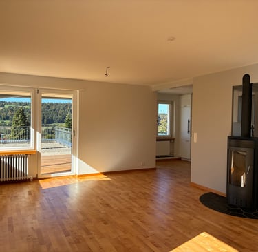 Spacious empty living room with hardwood floors, a modern black fireplace, and a balcony with a scenic mountain view.