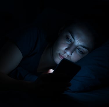 Realistic woman in bed in a dark room with her phone screen lighting up her face blue dimly