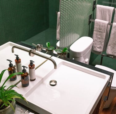 une salle de bain avec plan vasque design, carrelage mosaïque vert, toilettes et sèche serviettes