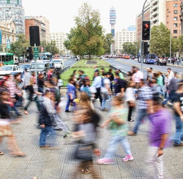 Pedestrians crossing a busy street. Cars, buses, other pedestrians, and buildings are visible in the background.