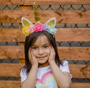 Little girl with hands on face wearing a unicorn headband