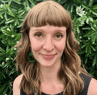 A white woman with a green earrings standing in front of a Passion Flower plant