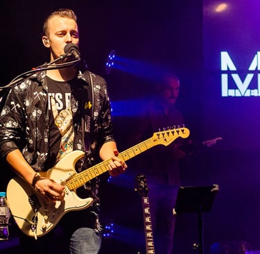 Guitarist and singer Lucas Vianna playing his white Fender Stratocaster guitar while singing.