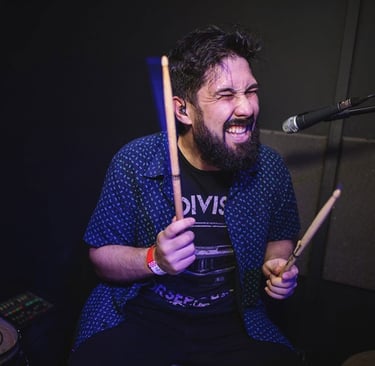 Drummer Lucas Dias playing the drums with his eyes closed, holding two drumsticks.