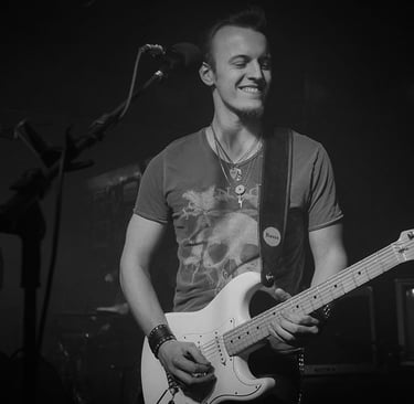 Guitarist and singer Lucas Vianna playing his white Fender Stratocaster guitar with his eyes closed and smiling.