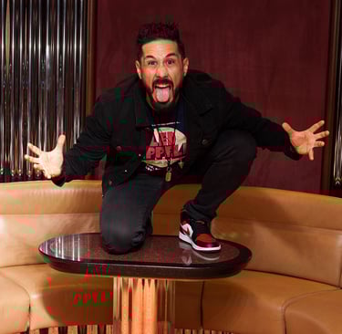 Drummer Lucas Dias crouching on a coffee table, making a funny pose and pulling a silly face.