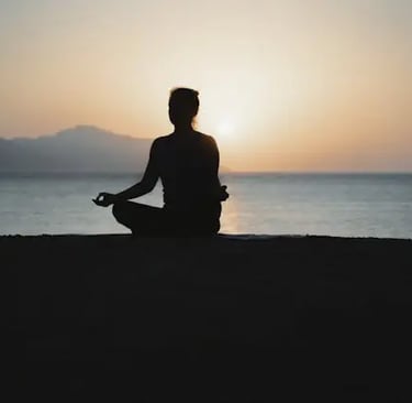 donna di spalle davanti al mare seduta in posizione yoga al tramonto