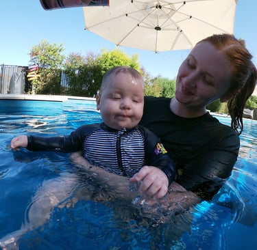 a woman in a swimsuit is holding a baby in a pool, preparing the baby for submersion