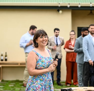 Laura smiles as she looks off camera. She is holding a microphone as she MC's a wedding
