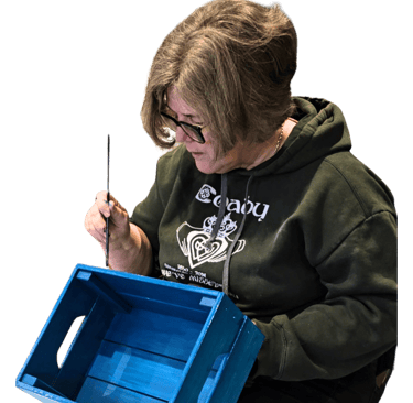 A lady painting a crate showing beginner level of furniture painting