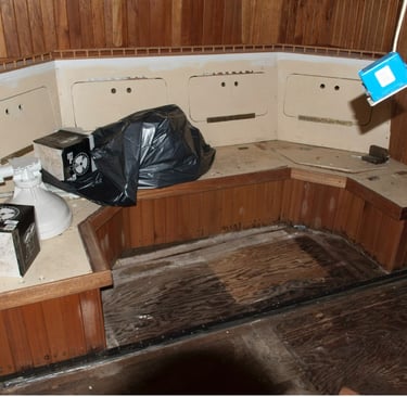 settee with some boat parts and a garbage bag on top in an unfinished interior made of wood