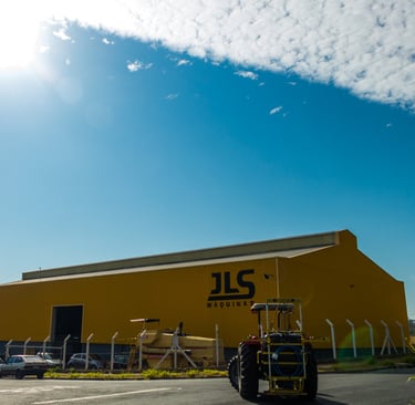 Pulverizador pecuário com a fábrica da JLS Máquinas ao fundo