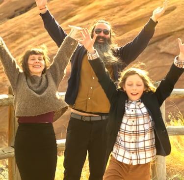 A family, mother father and son, throw their hands in the air at Red Rocks in Colorado