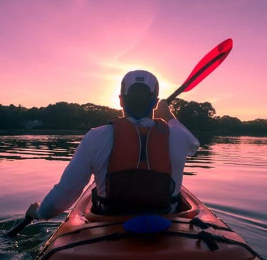 man paddling a kayak on a lake with the sun setting in the distance