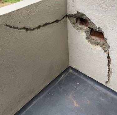 Mur de balcon fissuré avec éclatement partiel du crépi – état initial avant réparation.