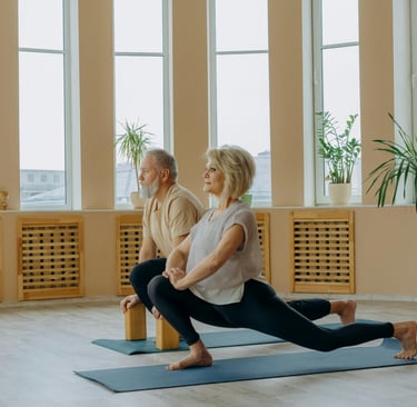Active senior couple practicing yoga lunges on mats in a bright wellness studio.