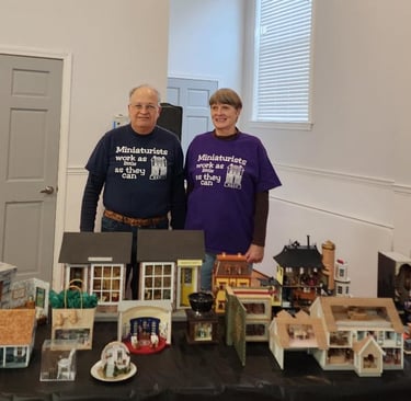 A picture of a man and woman with a table full of miniautre houses.