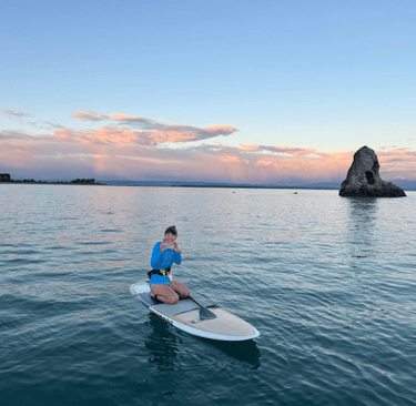 Woman on stand up paddle board on the ocean with a rock in the background