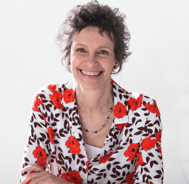 Une femme souriante, aux cheveux bruns et bouclés, elle porte un blazer fleuri, elle est sophrologue