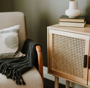 Un fauteil avec un plaid, à côté un vase et des livres posés sur un meuble en bois