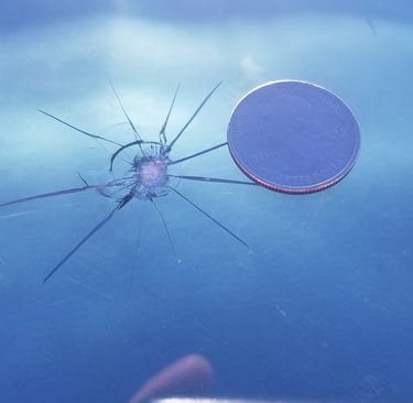 A star-shaped windshield crack next to a US quarter for scale, showing windshield damage requiring auto glass repair.