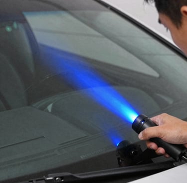 Technician uses a handheld UV lamp to cure resin during a professional car windshield chip repair.