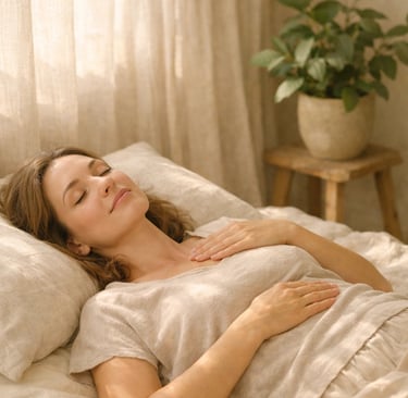 A peaceful woman deep breathing in a bed with linen sheets and sunlight streaming through curtains.
