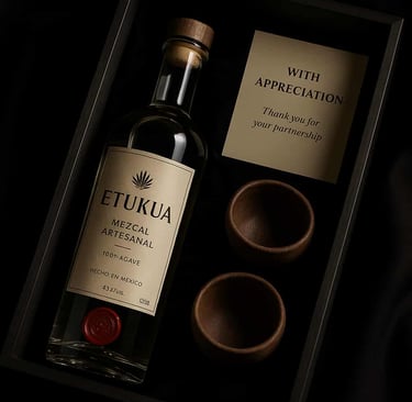 Caja regalo de lujo de Etukua abierta, mostrando una botella de mezcal artesanal con un lacre, dos c
