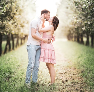 Couple kissing in a sunlit apple orchard during a romantic engagement photoshoot.