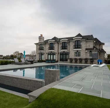 Luxury backyard with a modern geometric pool, stone patio, and a grand grey brick mansion.