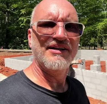 A man wearing sunglasses standing in front of a residential concrete block foundation at a construction site.