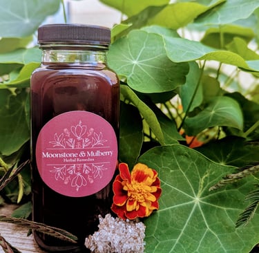 bottle of elderberry oxymel with leaves in the background and a marigold and crystal next to it
