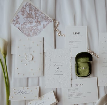 Elegant white wedding invitation suite with floral envelopes, pearl accents, and a green velvet ring box.