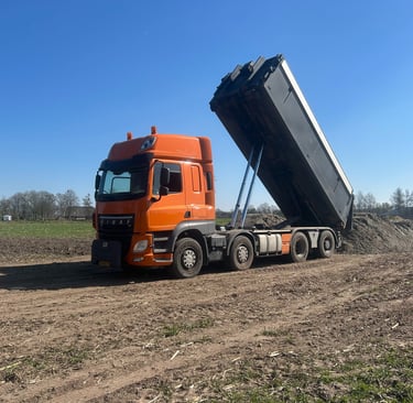 a dump truck with a dumpster sitting on the side of a dirt road