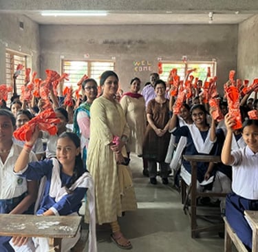 Large classroom of girls holding up napkin packs. with teachers