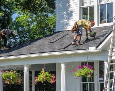 white house with a man ont he roof installing new roof tiles with a white ladder in the photo