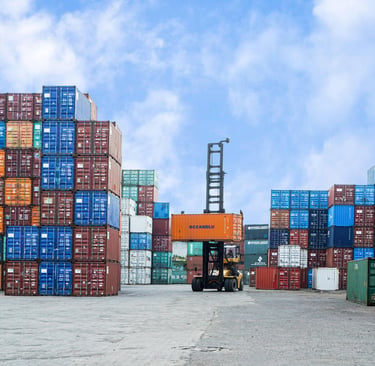 A forklift lifting a shipping container in a busy logistics terminal yard.