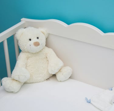 un lit bébé à barreaux et un doudou blancs dans une chambre aux murs bleus, pour une ambiance apaisante
