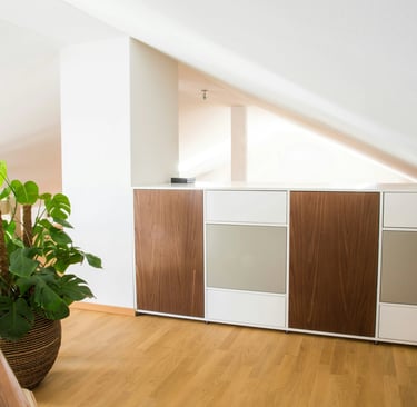 Mobilier blanc et bois foncé, mur blanc, parquet clair, plante verte dans pièce sous comble