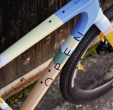 Close-up of a custom painted Open gravel bike frame with pastel color blocking and carbon wheels.