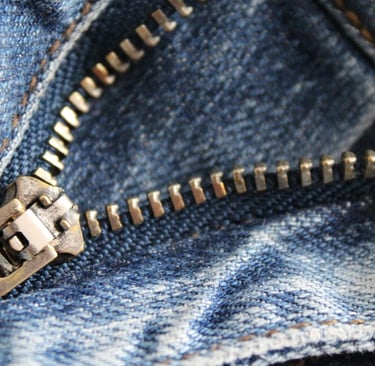 Close-up of a partially unzipped metal zipper on blue denim jeans.