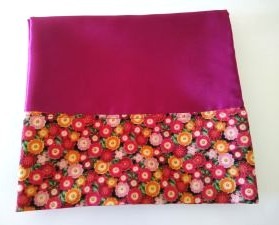 A burgundy satin pillowcase hemmed with floral trim on a white background.