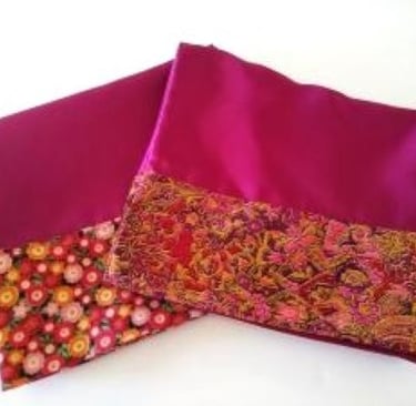 Two burgundy satin pillowcases hemmed with floral trim on a white background.