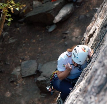 Person biting a cam while looking down and climbing a rock face. Photo credit: Brynn Weigelt.