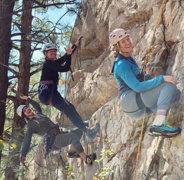 A group of three people smiling and hanging off ropes on an outdoor rock climb