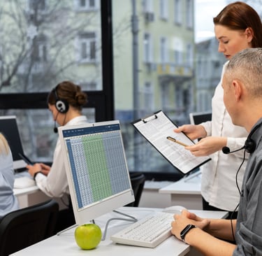 Tim HR mengelola data karyawan melalui HRMS software, dengan seorang staf memberikan laporan cetak kepada rekan kerjanya.